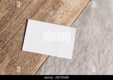 Closeup of blank business card on teak wooden table. Blurred beige linen background. Empty paper card mockup scene in neutral colors. Branding Stock Photo