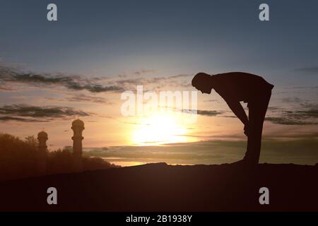 Silhouette of Muslim man in praying position (salat) with a sunset sky background Stock Photo