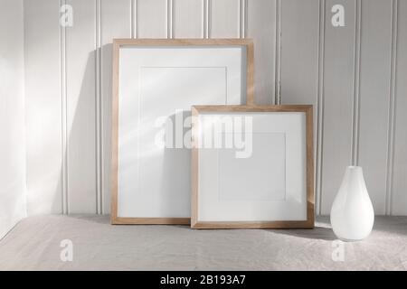 Two portrait and square wooden frame mockups. Linen cloth and modern ceramic vase with in sunlight. White beadboard wainscot wall paneling background Stock Photo