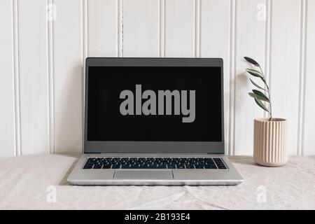 Feminine modern sparse workspace composition. Notebook mock-up scene. Pink ceramic vase with olive branch and laptop on beige linen tablecloth Stock Photo