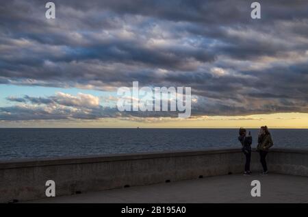 Two young girls photograph themselves near the sea under a cloudy sky Stock Photo