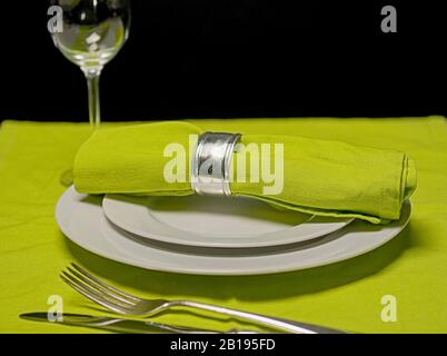 table setting with focus on napkin with silverware and glass on green table cloth Stock Photo