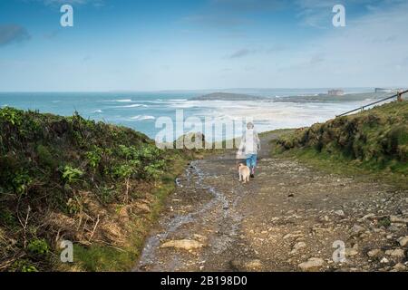 A woman taking her pet dog walking on a rugged coastal path on a cold windy day in Newquay in Cornwall. Stock Photo