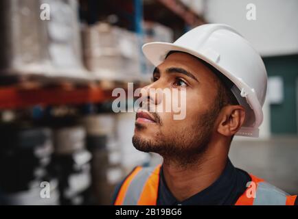 Side close-up of thoughtful african american male worker looking at copy space in warehouse wearing a white helmet Stock Photo