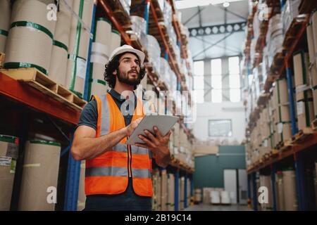 Concentrated successful warehouse manager inspecting inventory check from digital tablet while standing between shelf working Stock Photo