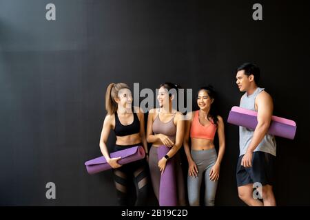 Happy smiling man and women having fun talking in gym. Group of young people relaxing in gym after workout training with black background. Stock Photo