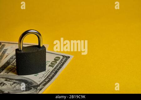 dollar banknotes and metal padlock at yellow background. Safety shopping, personal finances security, money savings concept. Stock Photo