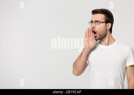 Millennial guy holding hand near mouth shouting, looking at copyspace. Stock Photo