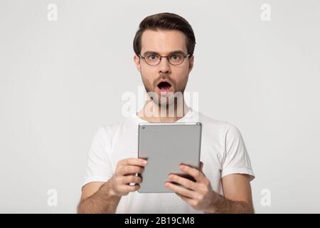 Surprised young man holding digital tablet, received unbelievable news. Stock Photo