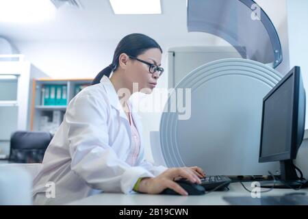 Dark-haired doctor in a white robe working on a computer looking concentrated Stock Photo