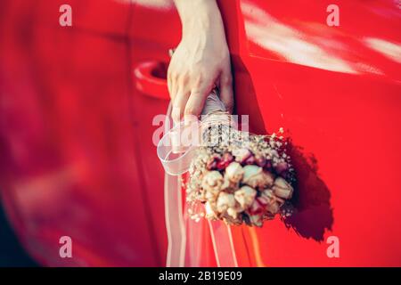 Bride holding the wedding bouquet and wave it from the window of the red car Stock Photo
