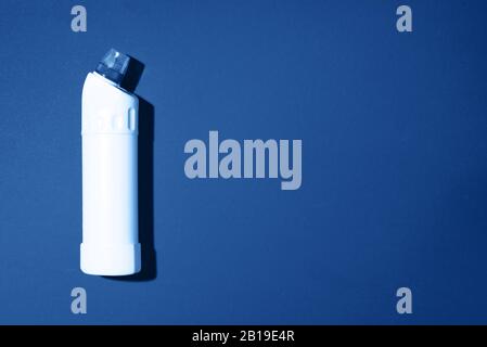 White plastic bottle of cleaning product, household chemicals or liquid laundry detergent on classic blue background. Top view. Flat lay. Copy space. Detergent bottle. Stock Photo
