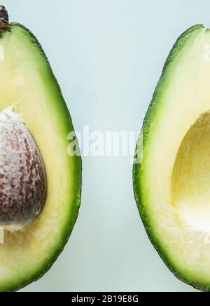 Ready to eat avocado cut into two halves, isolated on light green background. Stock Photo