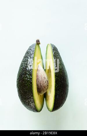 Ready to eat avocado cut into two halves, isolated on light green background. Stock Photo