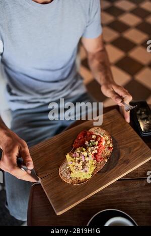 Closeup of young man eating italian bruschetta with coffee in cafe holding fork and knife Stock Photo