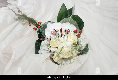Bouquet of white roses with orchids and red berries. on white cloth. Orchidaceae. Stock Photo