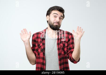 negligence concept. Young hispanic bearded man expressing carefree responsibility for childish mistake, studio shot. Not my problem at all. Stock Photo
