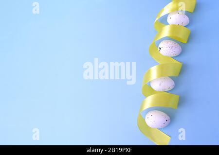 Easter right side border, white quail eggs with yellow ribbon on pastel blue background. Copy space for text. View from the top. Stock Photo