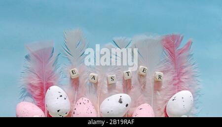 Flat lay composition easter pink eggs with feathers on mint backdrop. Greeting card or banner design. Stock Photo