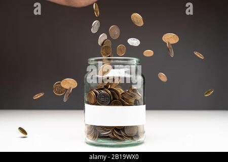 Coins in a jar with blank white label. Money falling from the sky above. Savings abstract concept. Copy space. Stock Photo