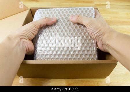 hand of man hold Bubbles covering the box by bubble wrap for protection product cracked  or insurance During transit - Stock Photo