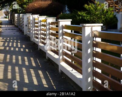 White stucco fence piers with horizontal brown metal slats. front yard. light modern fence along sidewalk. mediterranean type green garden. shadows. Stock Photo