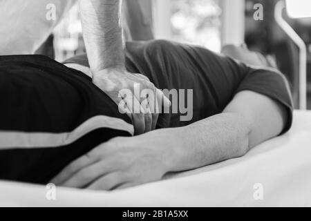 A man receiving relaxing massage therapy in the spa center. Black and white image of unrecognizable masseur hands doing massage Stock Photo