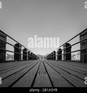 Wooden Pier. Low angle view of a wooden pier stretching out into the distance. Black and white process with added grain texture and copy space. Stock Photo