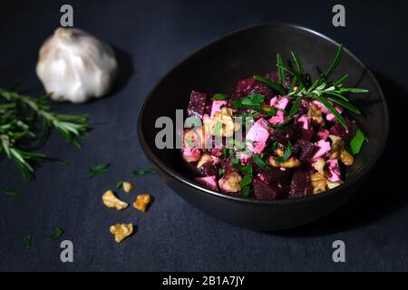 Beetroot salad with feta cheese and walnuts arranged in a brown ceramic bowl on black slate decorated with parsley Stock Photo