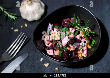 Beetroot salad with feta cheese and walnuts arranged in a brown ceramic bowl on black slate decorated with parsley Stock Photo