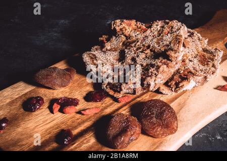 Homemade fruit bread on wooden chopping board with scattered dry berries on background on black table. Stock Photo