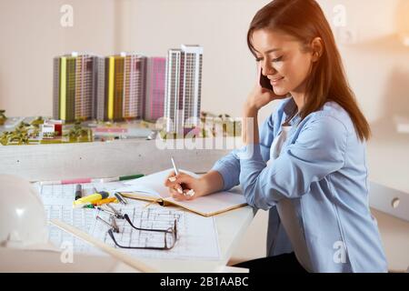 smiling good looking woman making notes while talking with her boyfriend by the smart phone, close up side view photo. consultation.discussion Stock Photo
