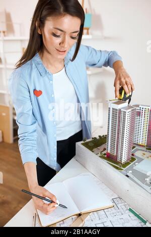 Closeup image of beautiful professional architect measures scale of a mass model on table in office, vertical shot. awesome designer working in office Stock Photo