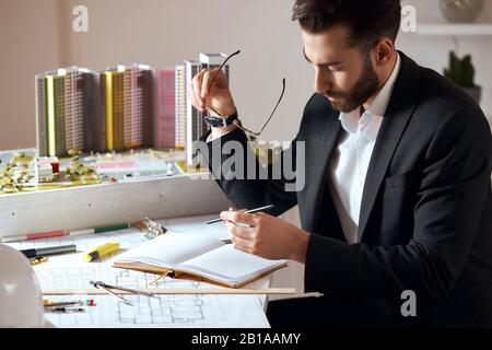 bearded good looking skilled architect making notes on notepad, close up side view photo.working time in the office.professional achitect developing i Stock Photo