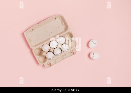 Happy Easter. White eggs with eyes in paper packaging on pink background. Flat lay, top view, copy space. Stock Photo