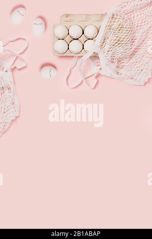 Happy Easter. White eggs with painted eyes in paper packaging and white mesh bag on pink background. Flat lay, top view, copy space. Stock Photo