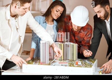 young engineers discussing apartment renovation idea at meeting, blonde man showing architectural plan to co-workers Stock Photo