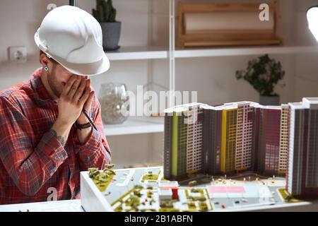 depressed tired architect closing his eyes with arms, coverying the face with palms. man hs a headache, sickness, illness , close up photo Stock Photo