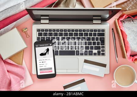 Online store for women on smart phone screen over pink desk table with laptop, credit cards and clothes. Top view. Stock Photo