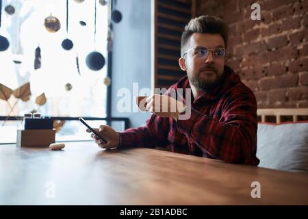 young clever man looking aside while working with smart phone, guy waiting for a woman who is being late, waitness, date Stock Photo