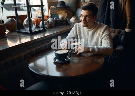 Young handsome thoughtful pensive man with a cup of coffee waiting for his girlfriend, close up photo, beauty, love, date Stock Photo