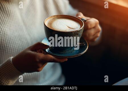 Hands of man holding a black cup of hot latte indoors, close up cropped side view photo. breakfast, relaxation, man having a rest at the cafe Stock Photo