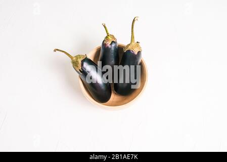 Three eggplants in a wooden bowl. Eggplant on a white background. Preparing for cooking. Flat lay, top view Stock Photo