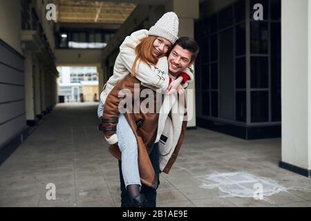 cheerful awesome guy giving piggyback ride to girlfriend, having fun in the city. close up portrait, love story Stock Photo