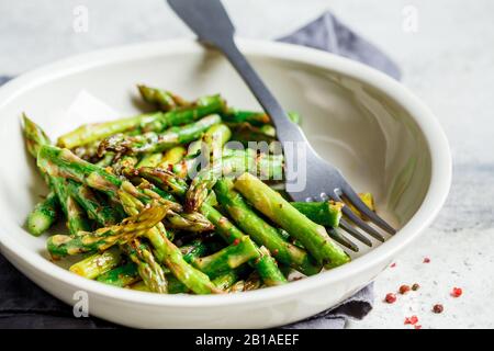 Green asparagus with pepper and salt in a white bowl. Stock Photo