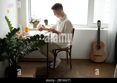 positive handsome student preparing for exam, guy is keen on his buisness. side view photo. journalist preparing a report at home , Stock Photo