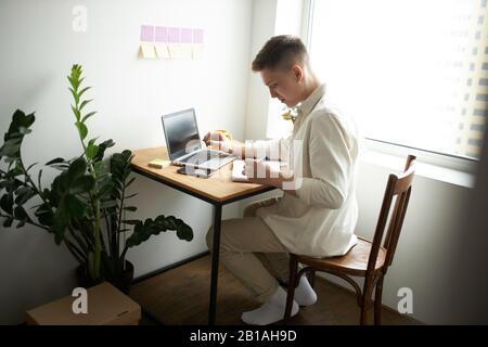 young journalist writing a report at home. close up side view photo. pleasant male designer writing on the notepad, notebook Stock Photo