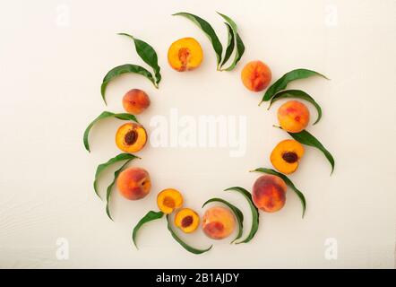 Peaches with leaves as frame on white wooden background. Circle made of peaches. Flat lay composition with ripe juicy peaches. Harvest of peaches for Stock Photo