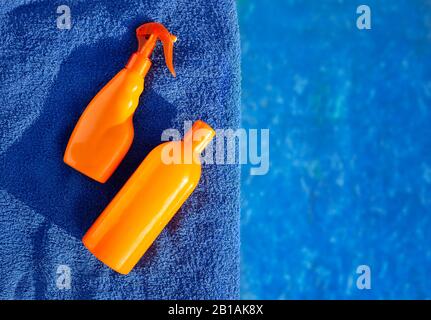 Cosmetic sunscreen products, set different orange bottles of sun protection body cream on blue towel against swimming pool. Skin care and protection Stock Photo