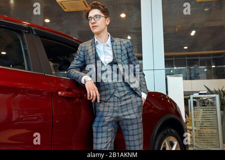 successful young man leaning on the modern luxury car and looking aside, close up side view photo. copy space.lifestyle, interest, job, work, professi Stock Photo